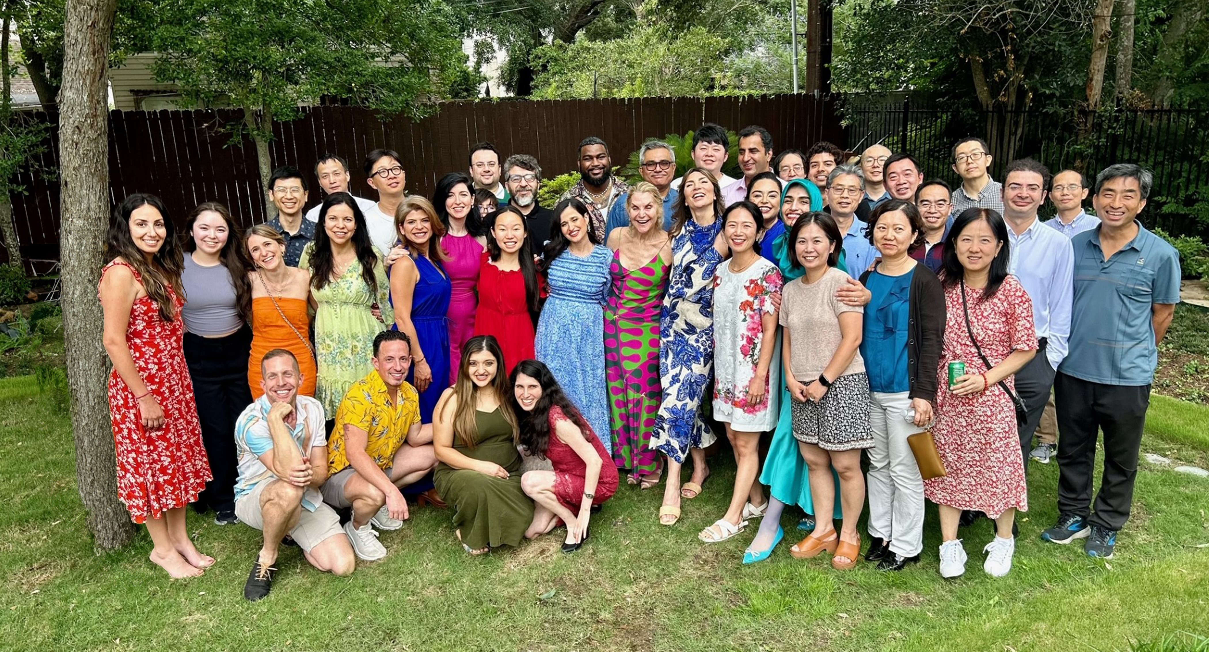 Large group photo of colleagues gathered outdoors in a backyard, standing and kneeling on the grass